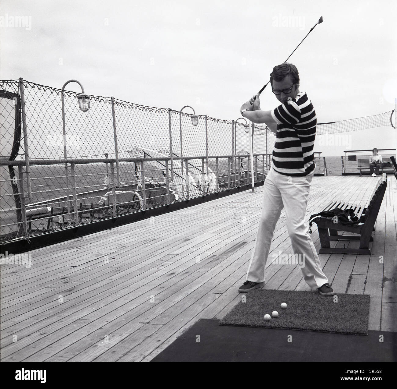 1960, historische, männliche Beifahrer auf dem Deck der Ocean Liner MS Sagafjord, üben seine Golf schlagen der Kugeln aus einem Gummi grass Mat. Stockfoto