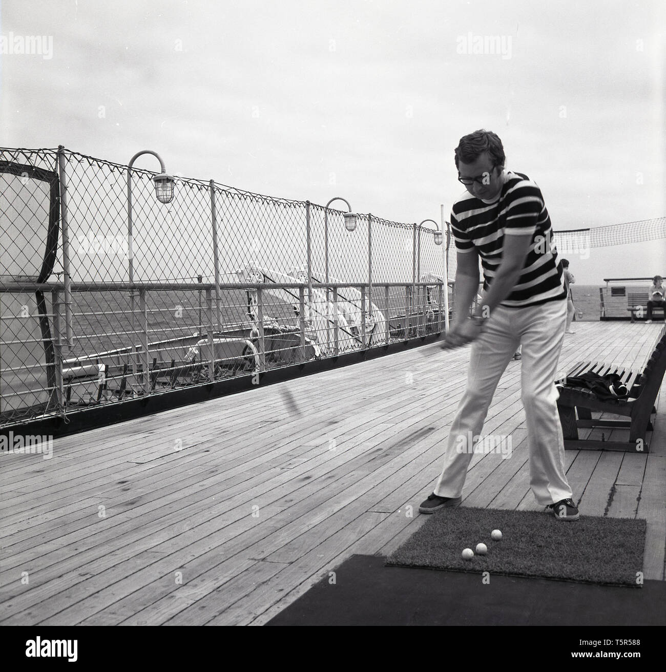 1960, historische, männliche Beifahrer auf dem Deck der Ocean Liner MS Sagafjord, üben seine Golf schlagen der Kugeln aus einem Gummi grass Mat. Stockfoto