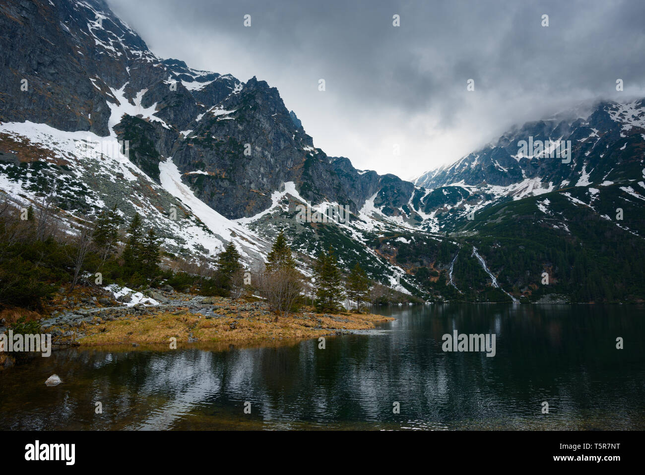 Berge mit Schnee und kleinen Wasserfällen zu einem See mit stürmischem Wetter fließt Stockfoto