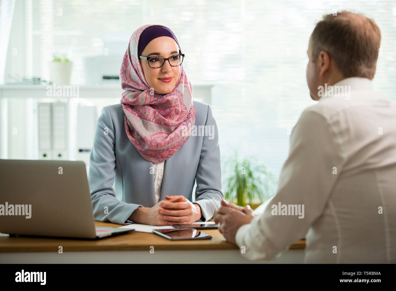 Mitarbeiter im Büro. Stilvolle Frau in Hijab, Gespräch am Schreibtisch mit Mann in Weiß moderne Büro. Muslimische Geschäftsfrau in Brillen Stockfoto Mitarbeiter im Büro. Stilvolle Frau in Hijab, Gespräch am Schreibtisch mit Mann in Weiß moderne Büro. Muslimische Geschäftsfrau in Brillen Stockfoto