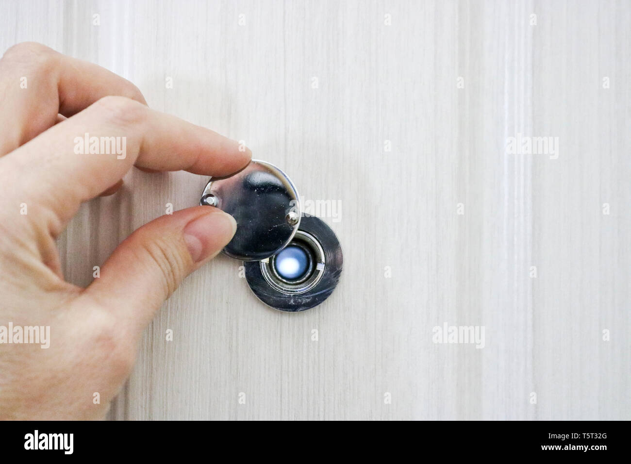 Die Hand öffnet die Tür Guckloch in der Tür von Eiche hell. Stockfoto