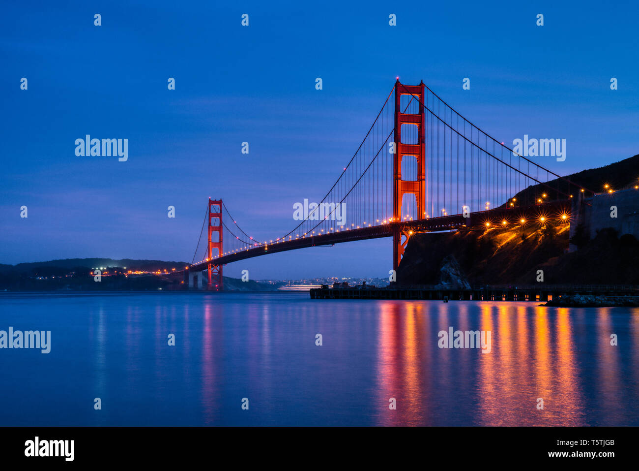 IconicGolden Gate Bridge bei blauer Stunde Nachtaufnahme mit Funkeln Lichter und friedliche ruhige Reflexion der Architektur launisch stilles Wasser Bay Area Stockfoto