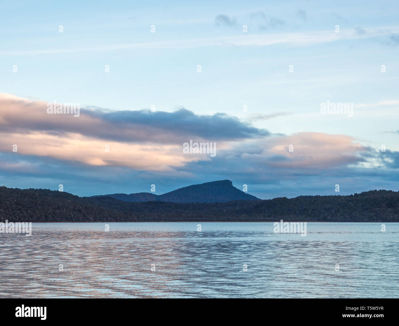 Eine Fernsicht, helle Wellen auf ruhigem Wasser, dunkle Hügel, unter Wolken in einen klaren Himmel, Lake Hauroko, Fiordland National Park, Southland, Neuseeland Stockfoto