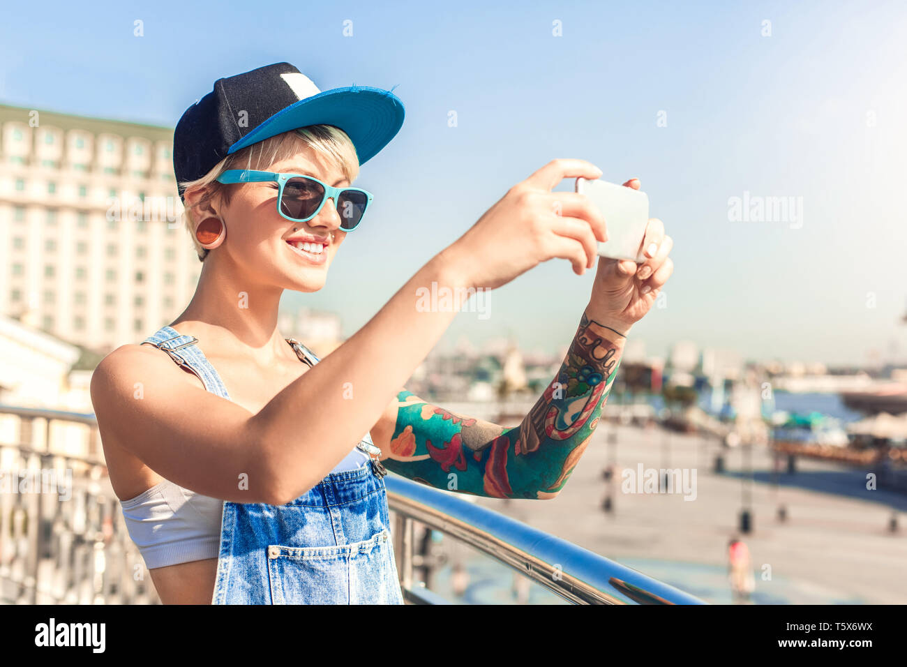 Junge alternative Mädchen mit Hut und Sonnenbrille auf der Straße der Stadt, Foto auf dem Smartphone lächelt Fröhlich schöne Aussicht Stockfoto