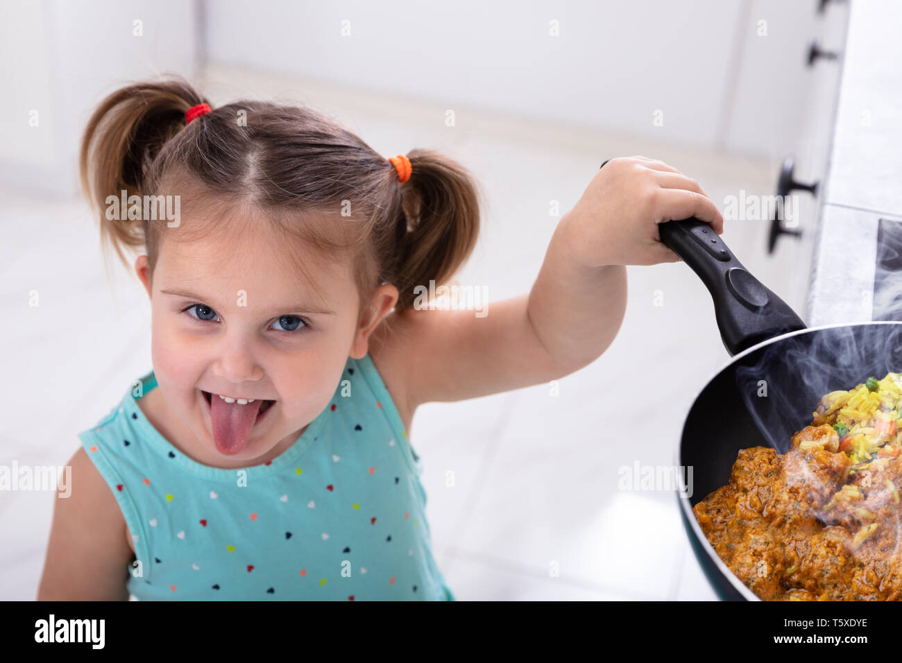 Lächelnd Kleine hübsche Mädchen, Mädchen spielen mit heißen Pfanne Kochen in der Küche Stockfoto