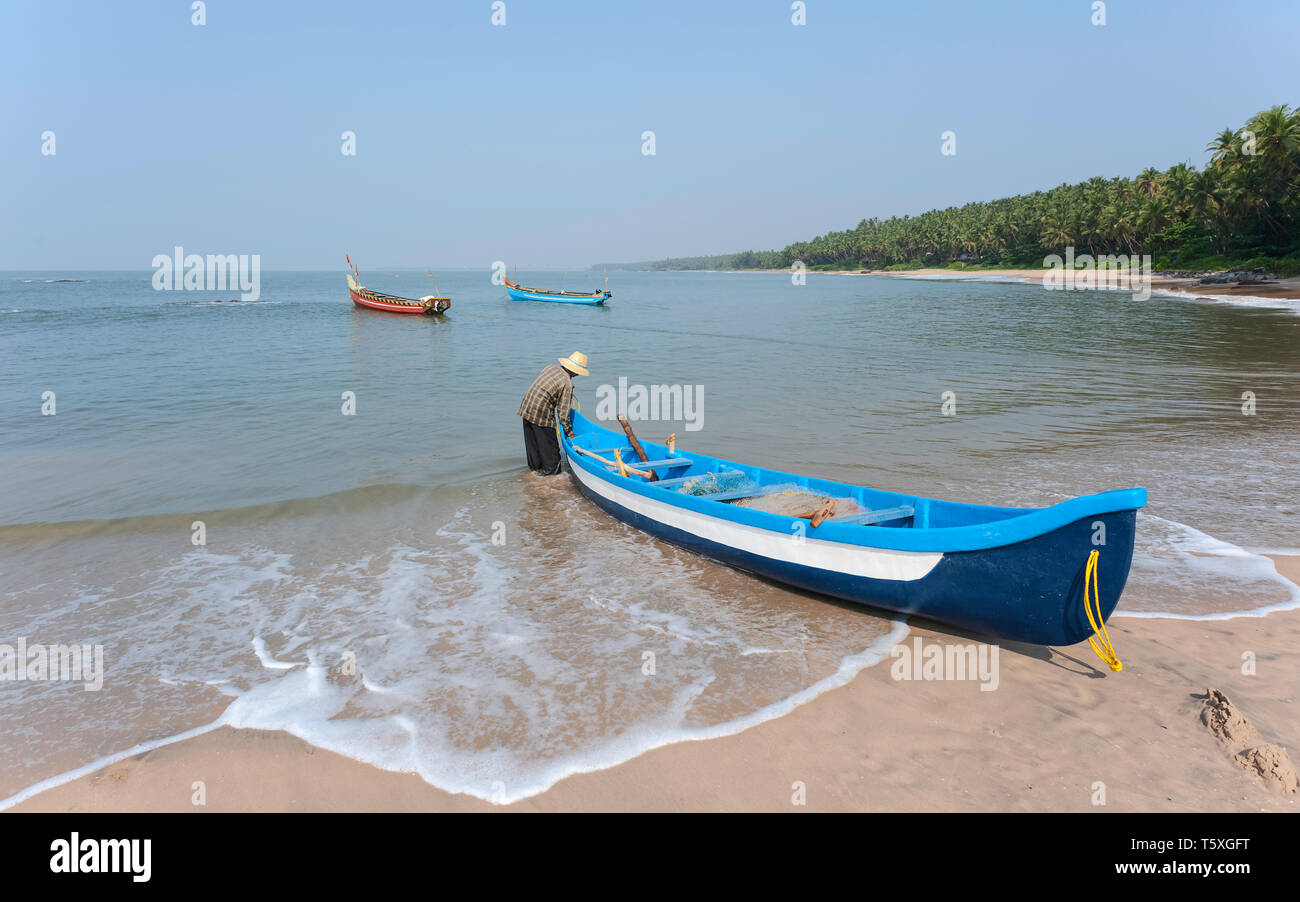 Nicht identifizierte Fischer neben Fischerboot auf Chera Strand (Thottada) zum Arabischen Meer an einem sonnigen Tag in Thottada, Kannur, Kerala, Indien. Stockfoto