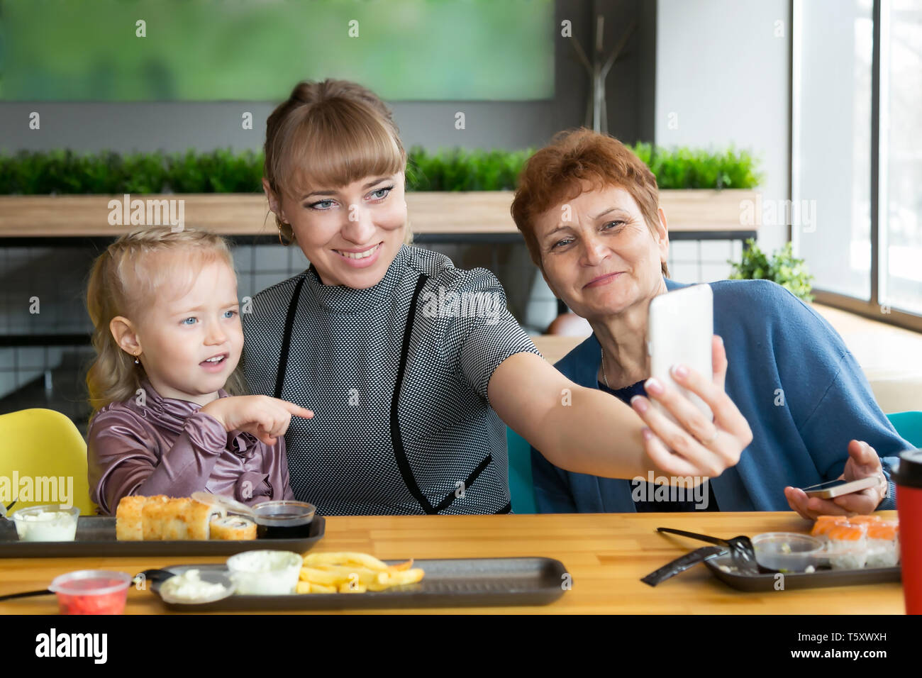 Eine junge Frau nimmt ein Bild von sich selbst auf einem Smartphone mit einem älteren Mutter und Tochter. Stockfoto