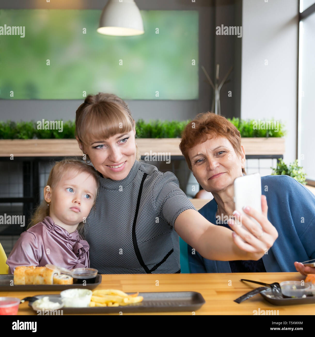 Eine junge Frau nimmt ein Bild von sich selbst auf einem Smartphone mit einem älteren Mutter und Tochter Stockfoto