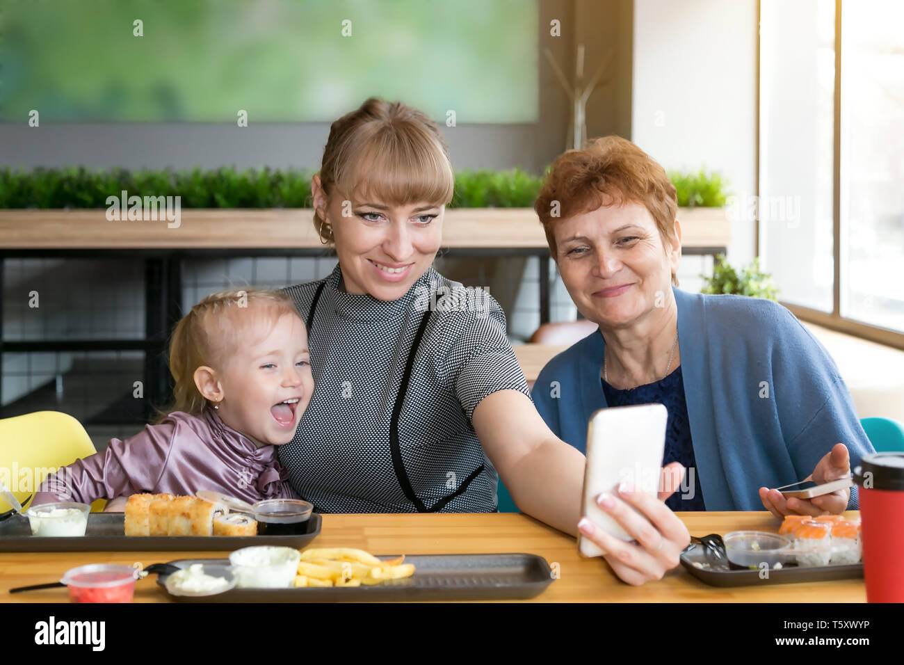 Eine junge Frau nimmt ein Bild von sich selbst auf dem Smartphone mit einer älteren Mutter und Tochter. Stockfoto