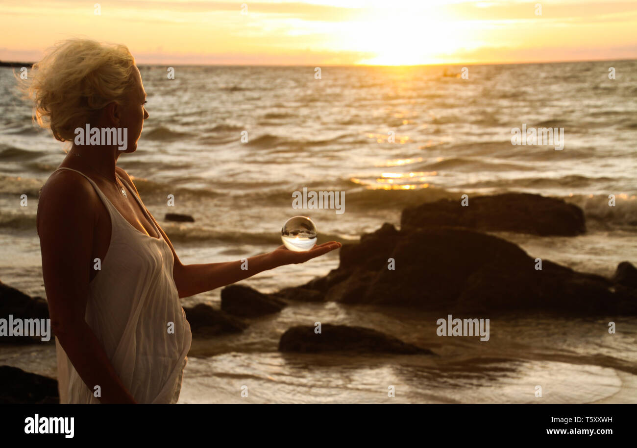 Blonde Frau in der Abendsonne Holding eine Kristallkugel auf Ko Lanta, Thailand Stockfoto