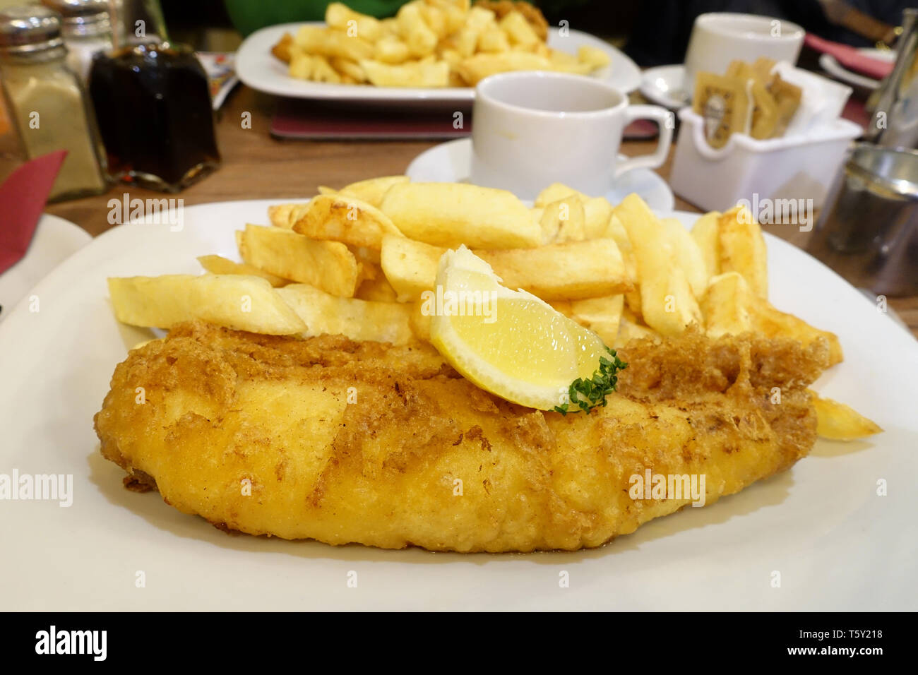 Ein traditioneller englischer Fisch und Chips essen serviert auf einem Tisch in einem Fisch und Chips Restaurant. Die Platten enthält frischen angeschlagenen Kabeljau, Chips und Kaffee Stockfoto