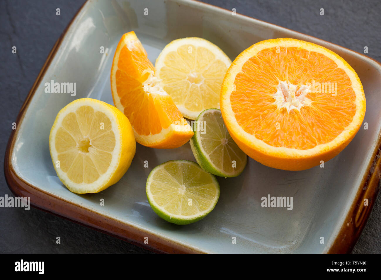 Eine Schüssel mit geschnittenen Zitronen, Limetten und Orangen, die für Aromastoffe ein Fischgericht verwendet wurden. Schiefer Hintergrund. Dorset England UK GB Stockfoto