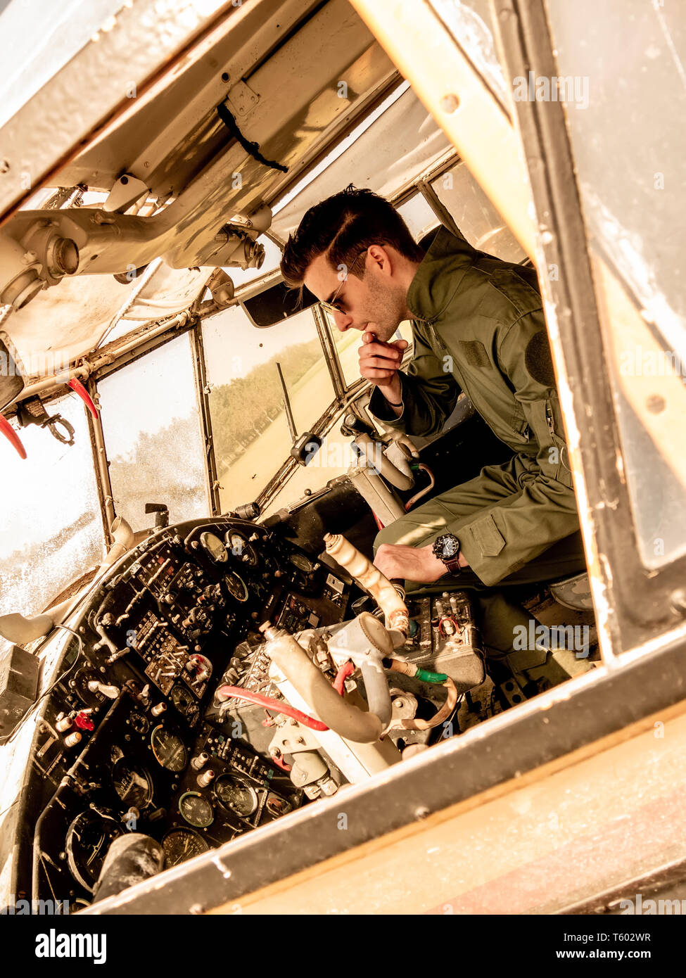 Ein hübscher junger Mann Pilot in einem grünen insgesamt im Cockpit eines alten Platanen an einem sonnigen Tag sitzen. Stockfoto