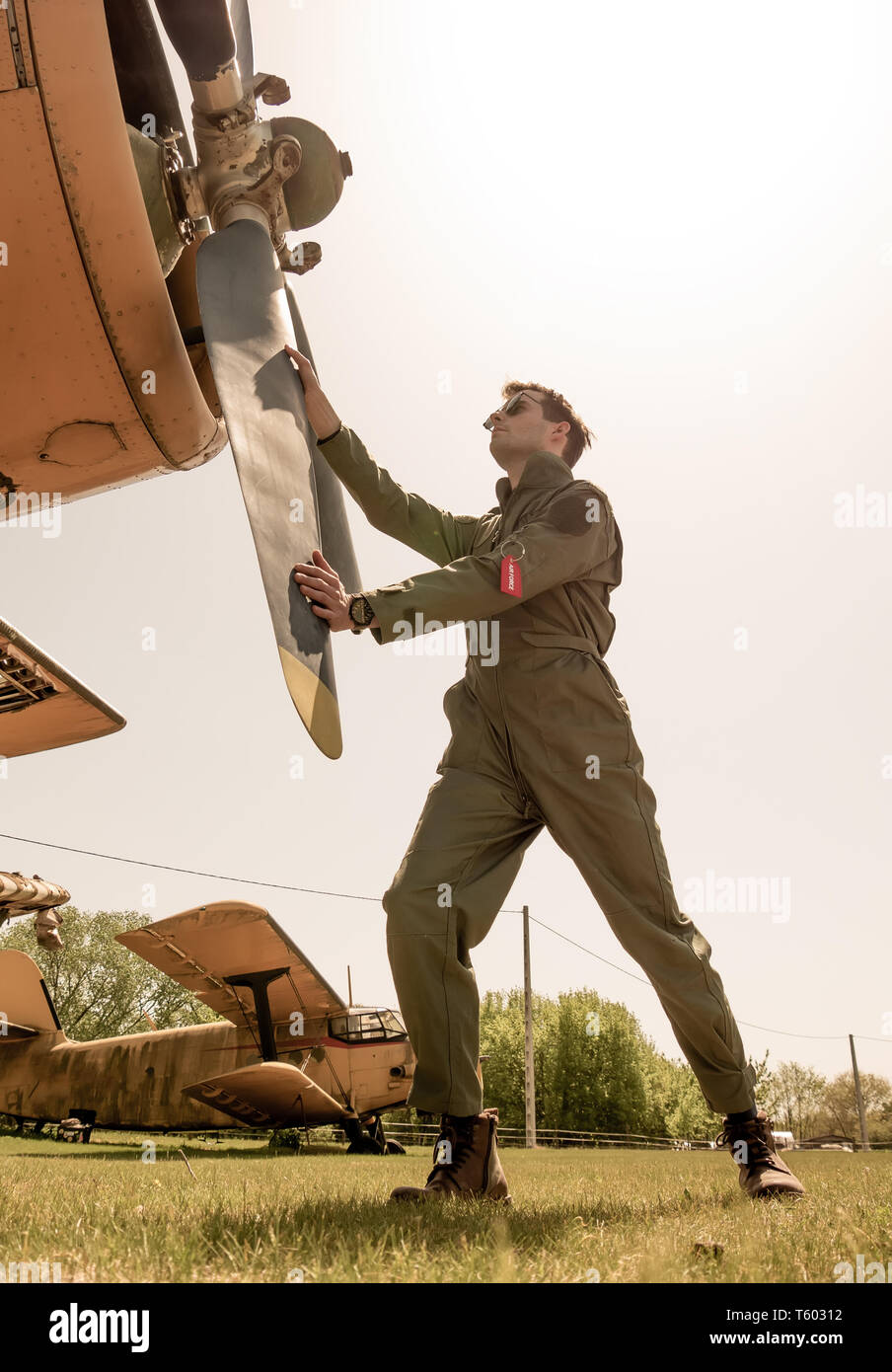 Ein hübscher junger Mann Pilot in einem grünen insgesamt Neben der Propeller eines alten Flugzeug an einem sonnigen Tag. Stockfoto