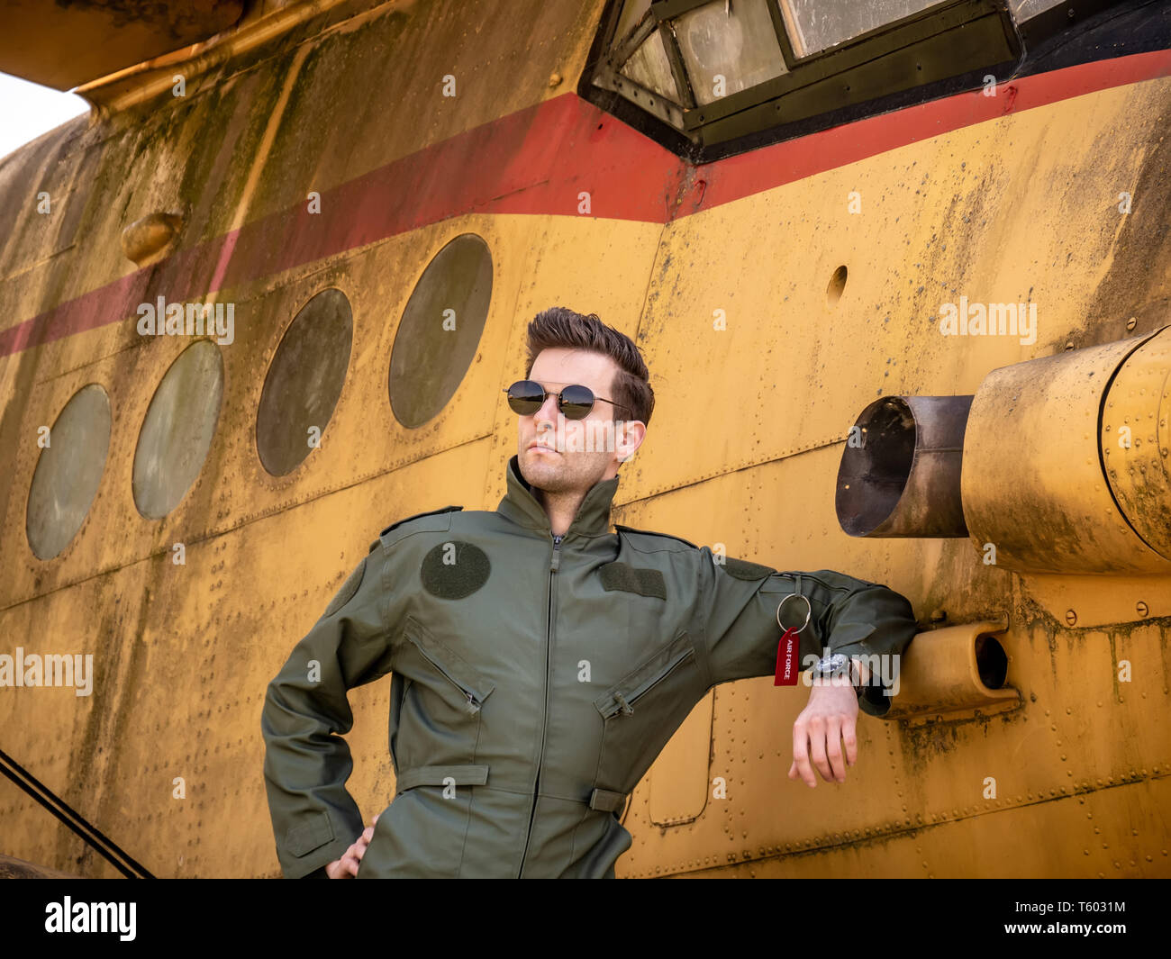 Ein hübscher junger Mann Pilot in einem grünen Insgesamt stehen neben einem alten Flugzeug an einem sonnigen Tag. Stockfoto