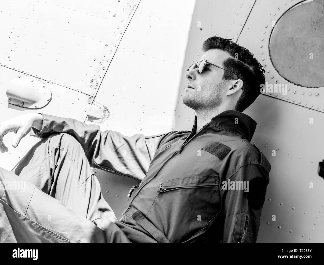 Ein hübscher junger Mann Pilot in einem grünen Insgesamt sitzen auf dem Flügel eines alten Platanen an einem sonnigen Tag. Stockfoto