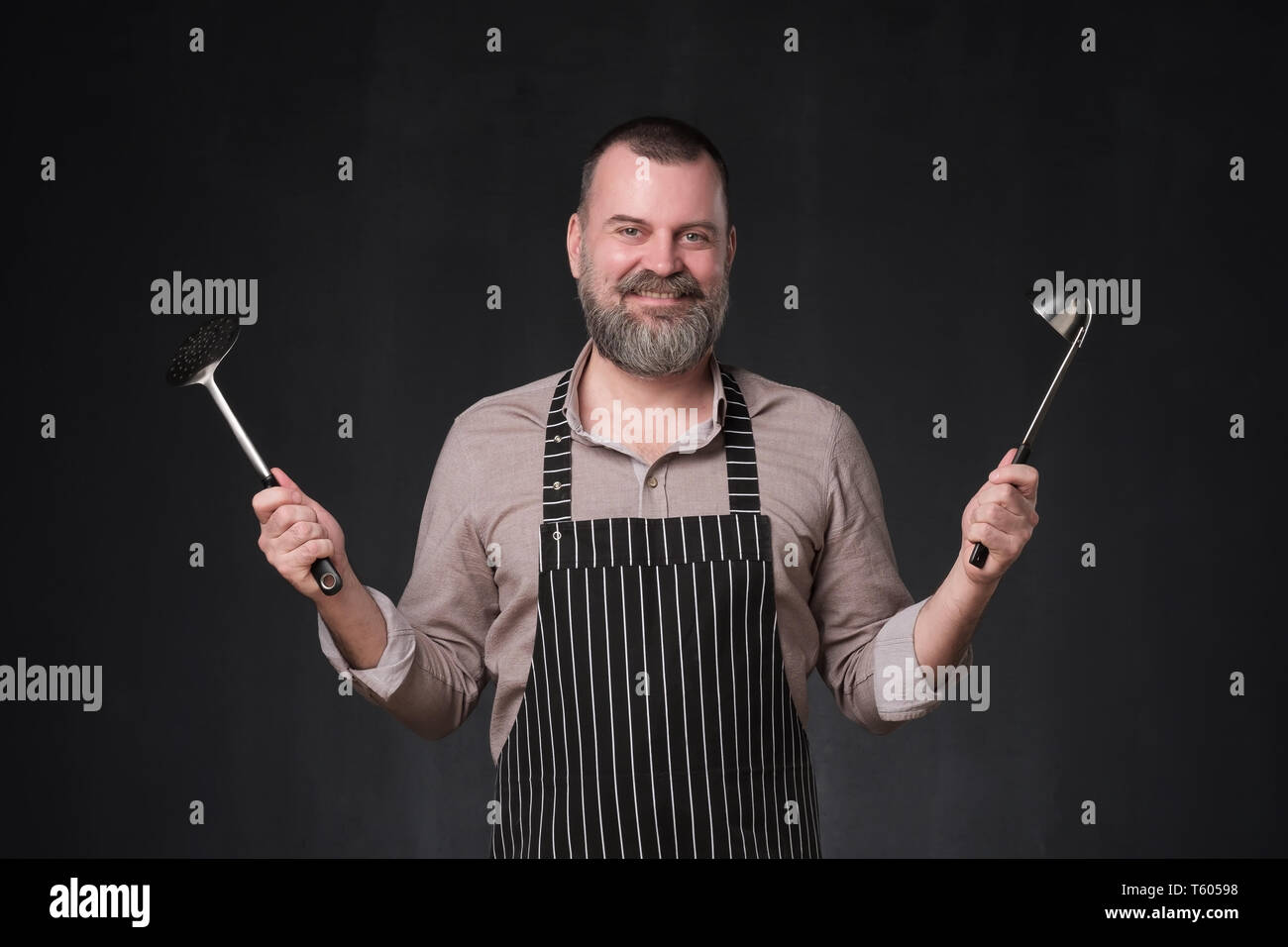 Reifen europäischen Chef mit Bart mit einer Schöpfkelle auf Schwarz studio Wand. Stockfoto