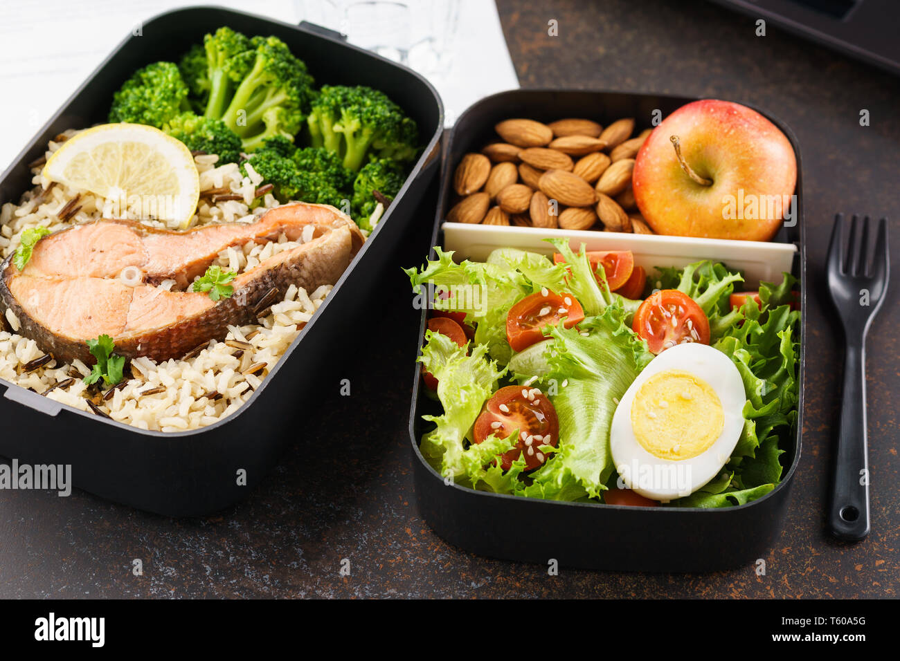 Gesundes Mittagessen im Büro Arbeitsplatz. Takeaway Lunch Boxen mit Ernährung Lebensmittel - Fisch, Gemüse und Obst an Schreibtisch mit Laptop. Stockfoto