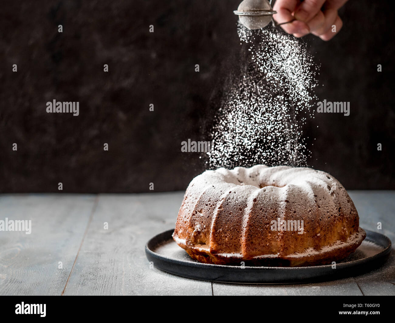 Woman's Hand bestreuen Puderzucker über frische Muffins Kuchen. Pulver Zucker fällt auf Frische perfekte muffin Kuchen. Kopieren Sie Platz für Text. Ideen und Rezepte für Frühstück oder Dessert Stockfoto