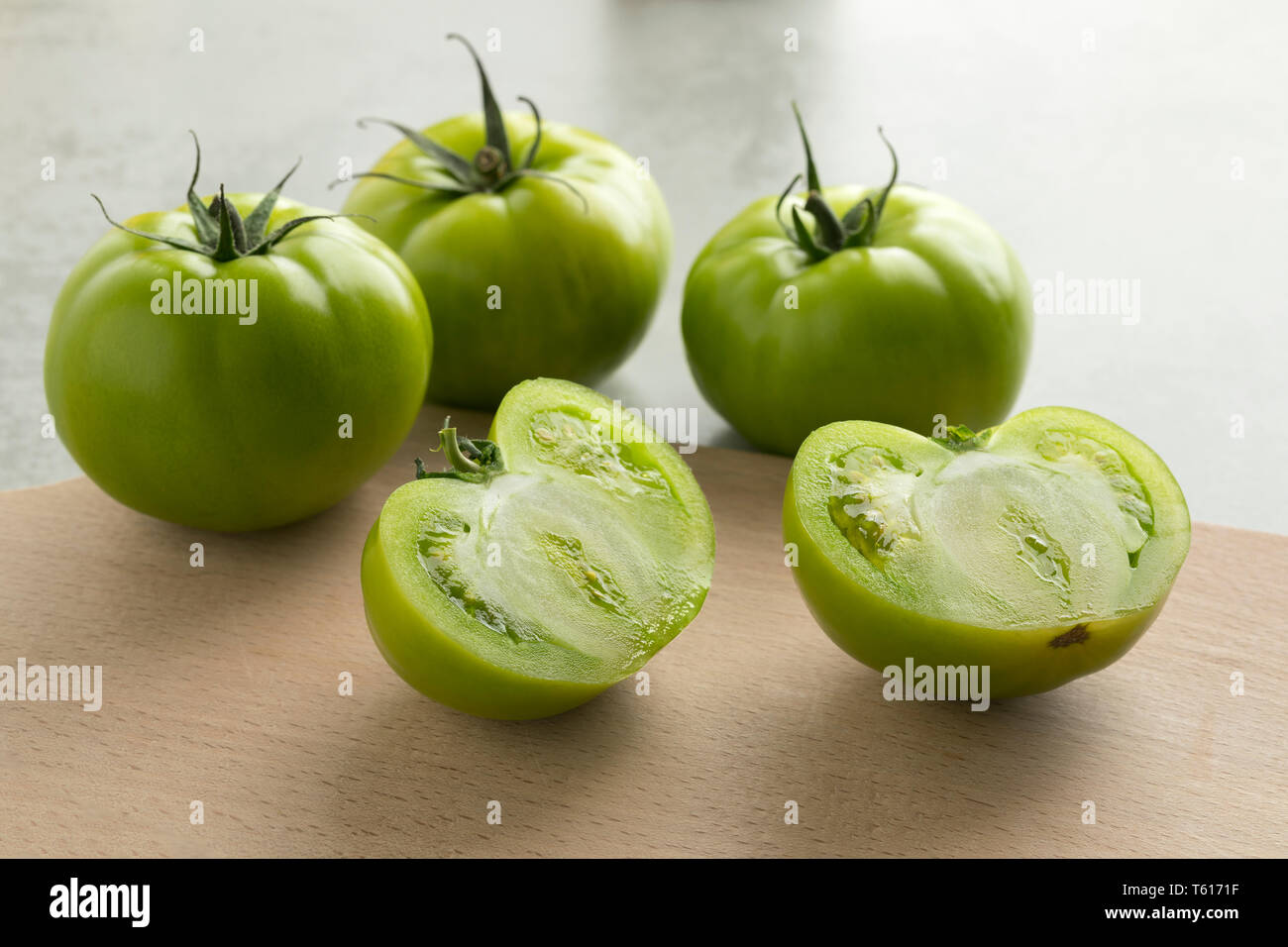 Ganze und halbe frische rohe grüne unreife Tomaten auf einem cutteing Board Stockfoto