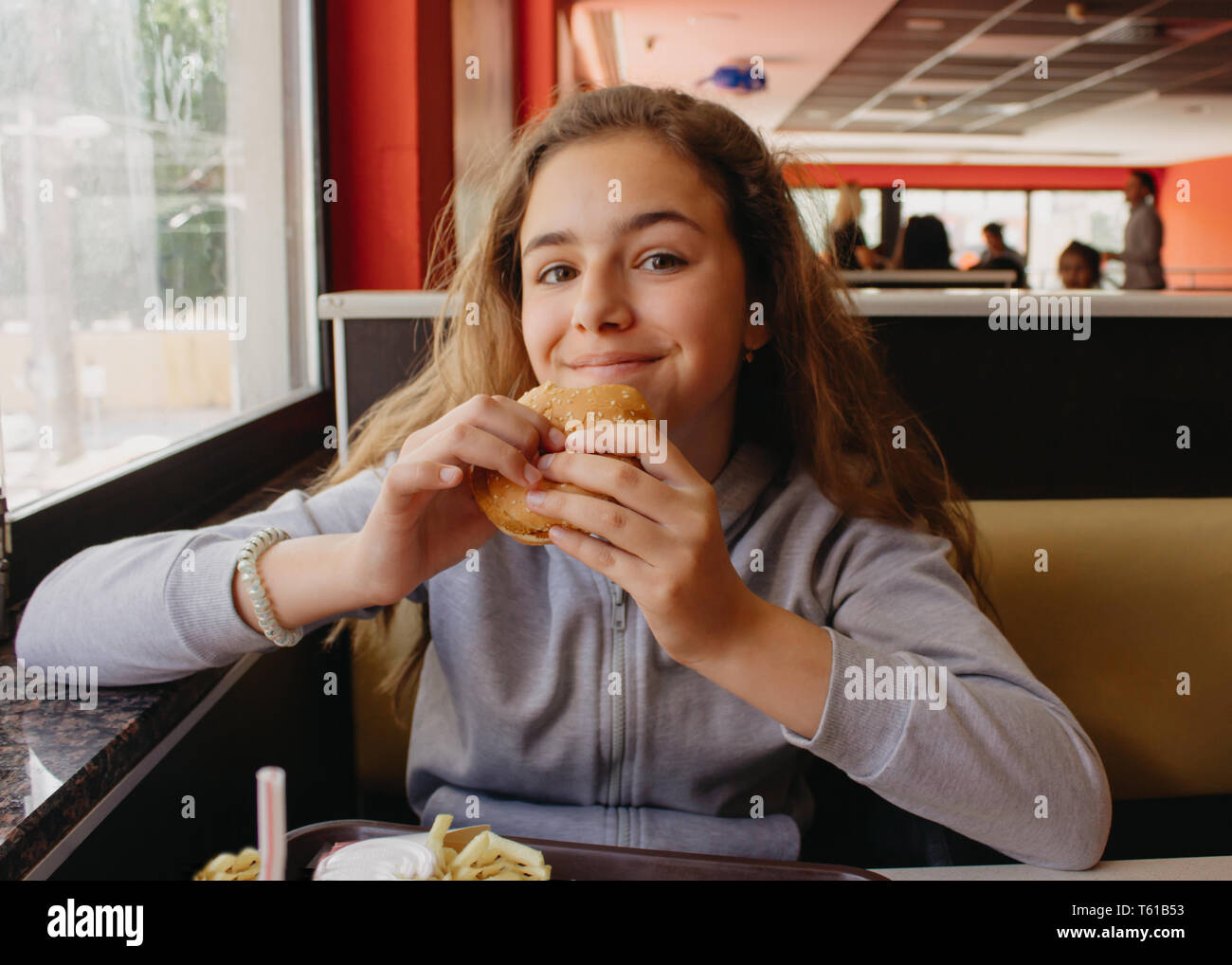 Hübsche, junge Teen Girl mit Appetit essen Hamburger in einem Cafe Stockfoto
