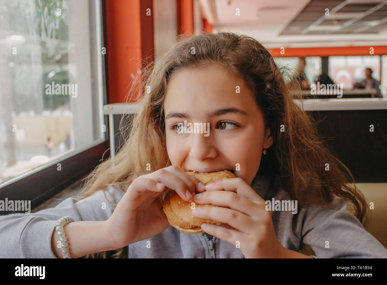 Hübsche, junge Teen Girl mit Appetit essen Hamburger in einem Cafe Stockfoto