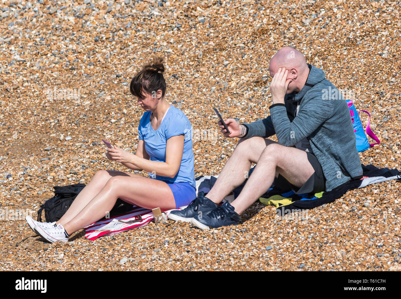 Paar Leute in ihrer 30. Sitzung am Strand an einem warmen Tag im Frühling, ignorieren einander während der Verwendung von Handys, in England, Großbritannien. Stockfoto