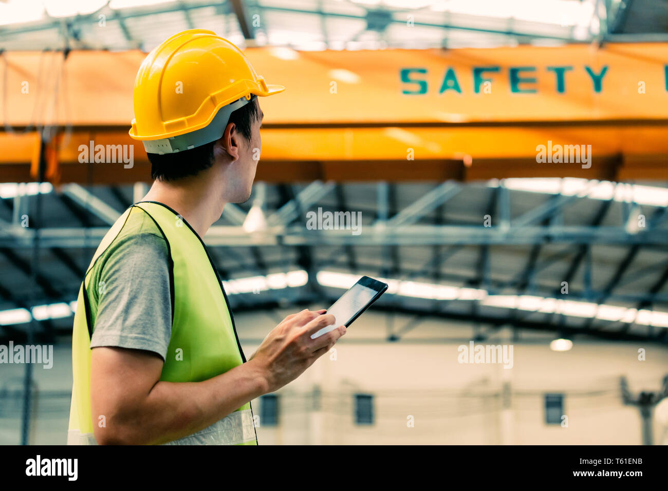Jungen asiatischen Männlich schwere allgemeine Arbeitnehmer mit einem digitalen Tablet in Fertigung und Fabrikgelände mit Kran hinter Stockfoto