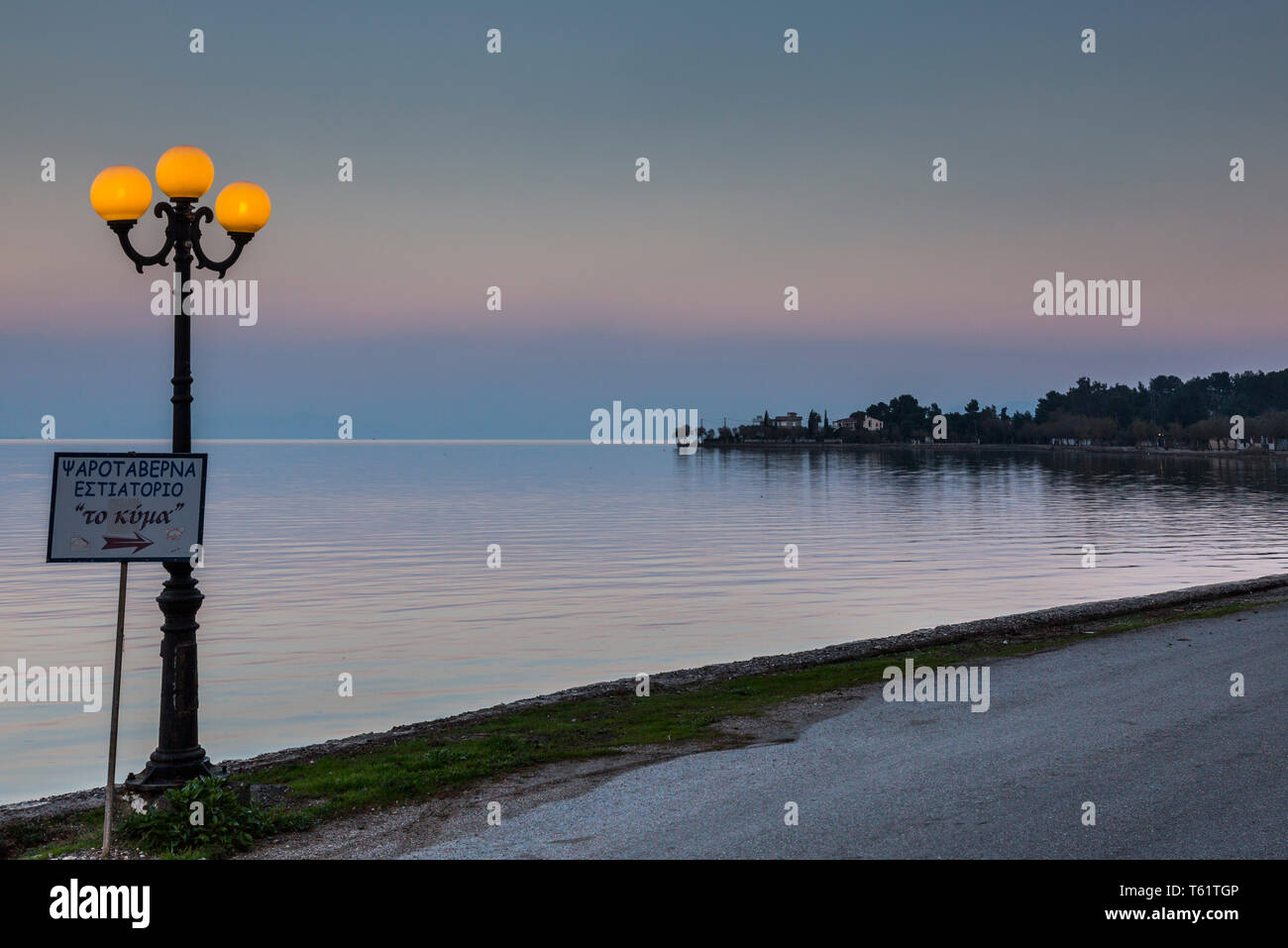 In der Ortschaft Avlida eine Straßenlaterne leuchtet gegen ein Abendhimmel neben ruhigen Wasser in den Golf von Euböa. Stockfoto
