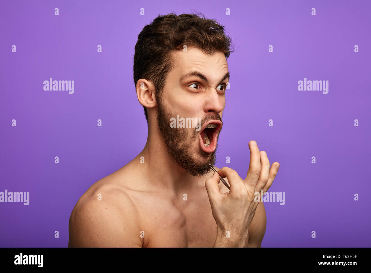 Ein Mensch, der leidet, zupfen seinen Bart Haar, über blau Hintergrund isoliert stehen, Nahaufnahme, Seite, Ansicht Foto. Man schreit, wie er Schmerz fühlt, während pl Stockfoto