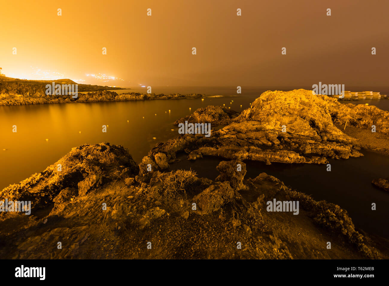 Nachts lange Exposition von einem Strand in Los Cancajos, La Palma, Spanien. Ansicht mit einigen Felsen und das intensive orange Licht von Santa Cruz im Hintergrund Stockfoto