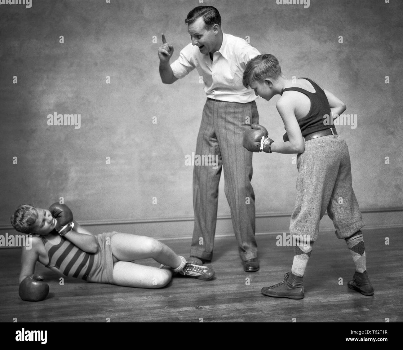 1930er Jahre zwei jungen SPARRING STANZEN VERPACKEN EIN junge KNOCKED DOWN MANN ALS SCHIEDSRICHTER ZÄHLEN IHN-b 8272 HAR 001 HARS ZUFRIEDENHEIT STUDIO SHOT GESUNDHEIT LEICHTATHLETIK KOPIE RAUM VOLLER LÄNGE KÖRPERLICHE FITNESS PERSONEN MÄNNER RISIKO ATHLETISCHE HANDELN B&W ABENTEUER SCHUTZ STÄRKE AUFREGUNG OUTFITS ERHOLUNG STOLZ STANZEN VERBINDUNG ATHLETEN ZUSAMMENARBEIT IHM JUGENDLICHE klopfte Mitte - Mitte - erwachsenen Mann SPAR SPARRING SCHWARZ UND WEISS KAUKASISCHEN ETHNIE HAR 001 ALTMODISCH Stockfoto