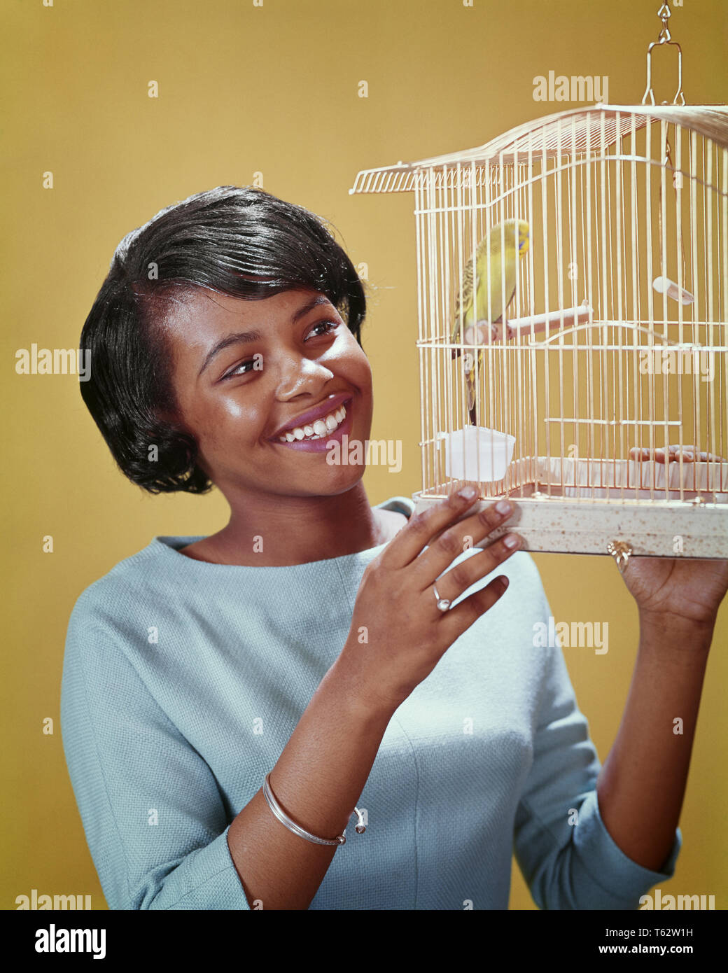 1960er lächelnd afrikanische amerikanische Frau auf der Suche nach PET-SITTICH IN EINEM VOGELKÄFIG - kb 9294 PHT 001 HARS KÄFIG FLÜGEL GLÜCK FRÖHLICH afrikanische Amerikaner afrikanisch-amerikanische SCHWARZ ETHNIZITÄT LÄCHELT VERBINDUNG SITTICH FREUDIGE WARMBLÜTIGER WIRBELTIERE FEATHERED GEFLÜGELTE JUNGE ERWACHSENE FRAU ZWEIBEINIGEN zur EIABLAGE ALTMODISCHE afrikanische Amerikaner Stockfoto