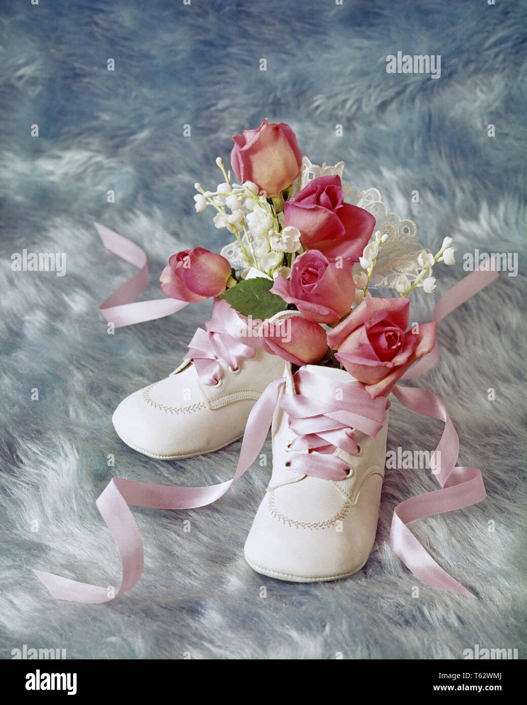 1970s 1980s Geburtstag noch LEBEN DER WEISSEN BABY SCHUHE HOLDING MINIATUR ROSA ROSEN UND BABY'S ATEM Blumen auf blau hintergrund-kf 8897 PHT 001 HARS ALTMODISCH Stockfoto