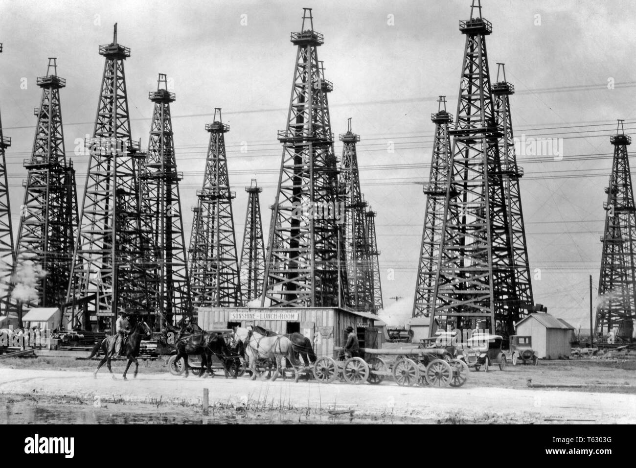 1900s SPINDLETOP HILL ÖLFELD ca. 1903 ÖLDERRICKKRÄNE UND MITTAGESSEN ZIMMER FUSSGÄNGER ARBEITNEHMER PFERDE WAGEN BEAUMONT TEXAS USA-q 74960 CPC 001 HARS KONZEPTIONELLEN TEIL WAGEN ENTFERNT BOOMTOWN GULF COAST BEAUMONT CA. SPINDLETOP SCHWARZ UND WEISS LADEBÄUMEN ÖLFELD ALTMODISCH Stockfoto