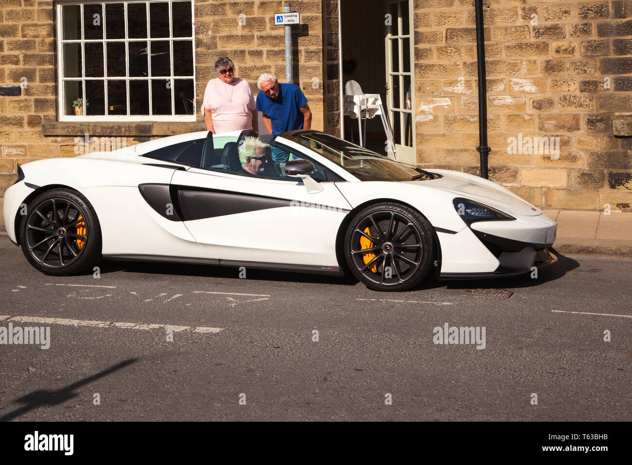 McLaren Sportwagen wird von älteren Mann angetrieben und bewundert von zwei Menschen am Straßenrand stehend Stockfoto