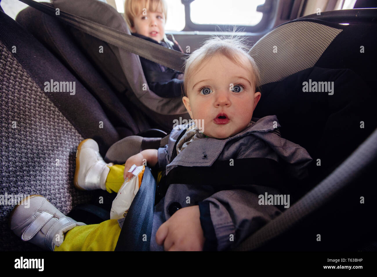 Ein Baby in der Sonnenbrille seiner Mutter sitzt in einem Auto in einem  Kindersitz und zeigt seine Zunge aus dem Fenster Stockfotografie - Alamy