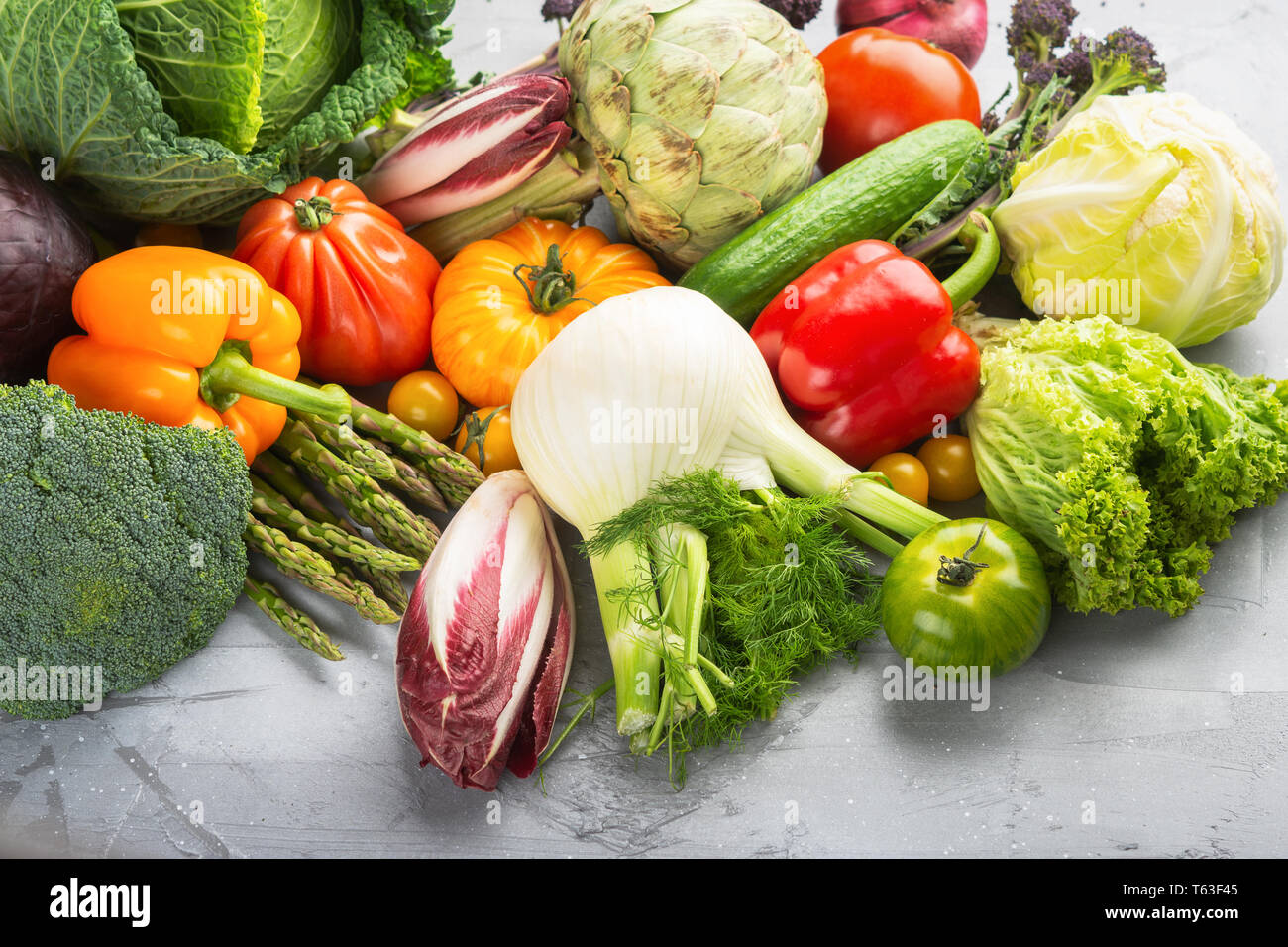Frisches rohes Gemüse, Kohl Karotten Pfeffer Fenchel Broccoli Spargel Tomaten Salat artichocke, auf Grau konkreten Hintergrund, selektiver Fokus Stockfoto