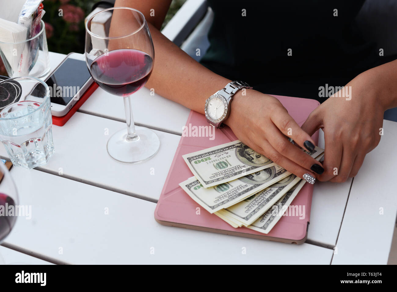 Geldscheine Dollar in die Hände eines Mädchens Geschäftsmann für den Kauf einer Zahlung, die in einem Restaurant an einem Tisch mit einer plaghet und einem Glas Wein sitzt Stockfoto