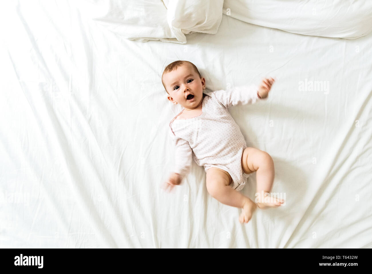 6 Monate alten Baby suchen Bei camera am Morgen auf dem Bett liegend zwischen weißen Laken. Stockfoto