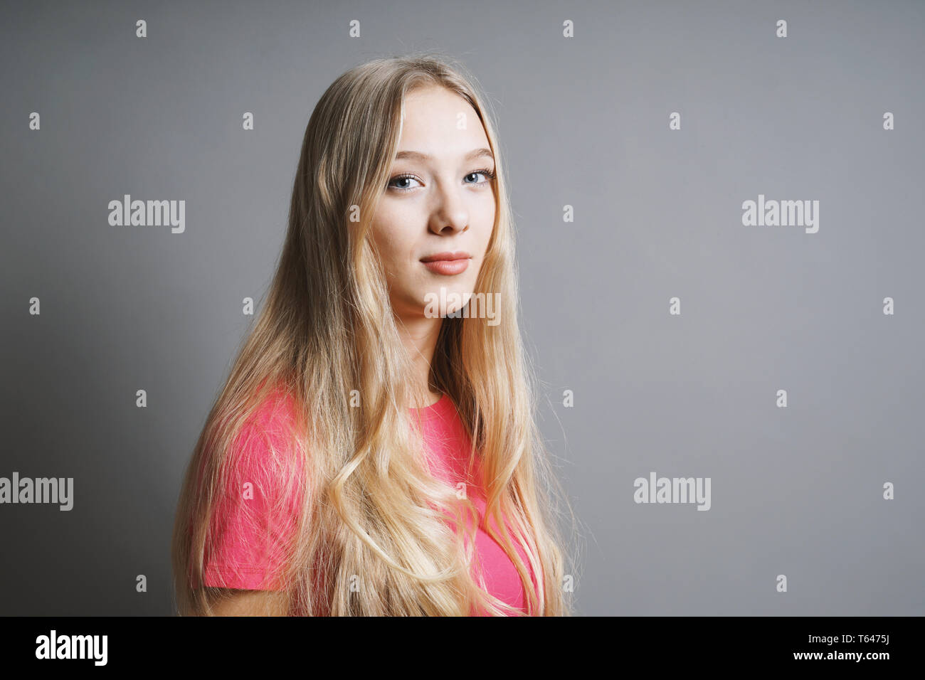 Sicher zufriedener junge Teenager Frau mit langen blonden Haaren und rosa-t-shirt gegen grauen Hintergrund mit Kopie Raum Stockfoto
