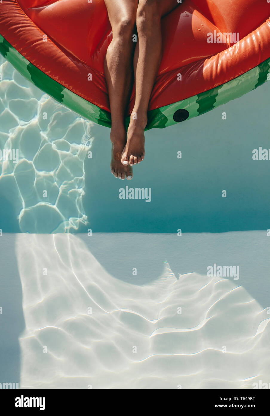 7/8 Schuß von Frau Beine auf eine schwimmende Matratze im Schwimmbad. Weibliche Sonnenbaden auf aufblasbaren Matratze im Pool. Stockfoto