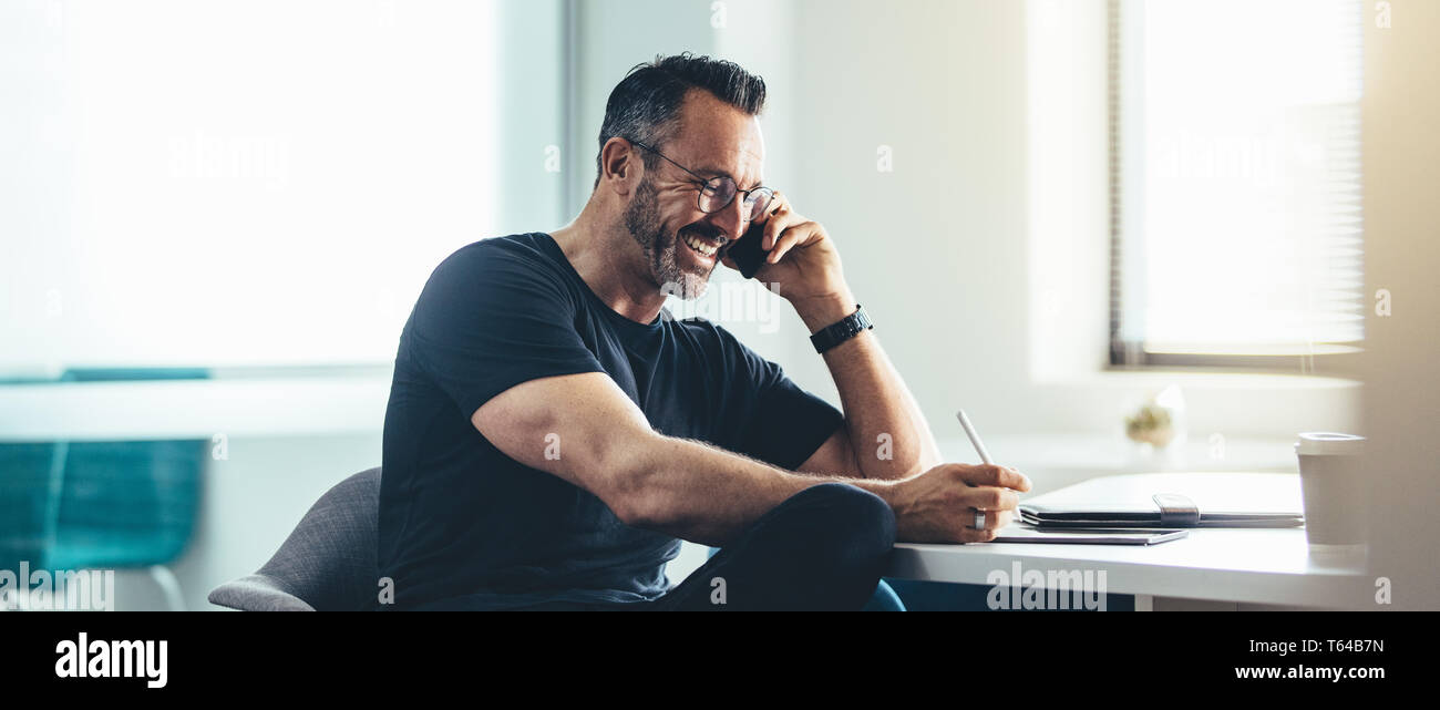 Lächelnd Mann bei der Arbeit mit Handy und der Arbeit an seinem digitalen Tablet. Freundliche Unternehmer arbeiten im Büro. Stockfoto