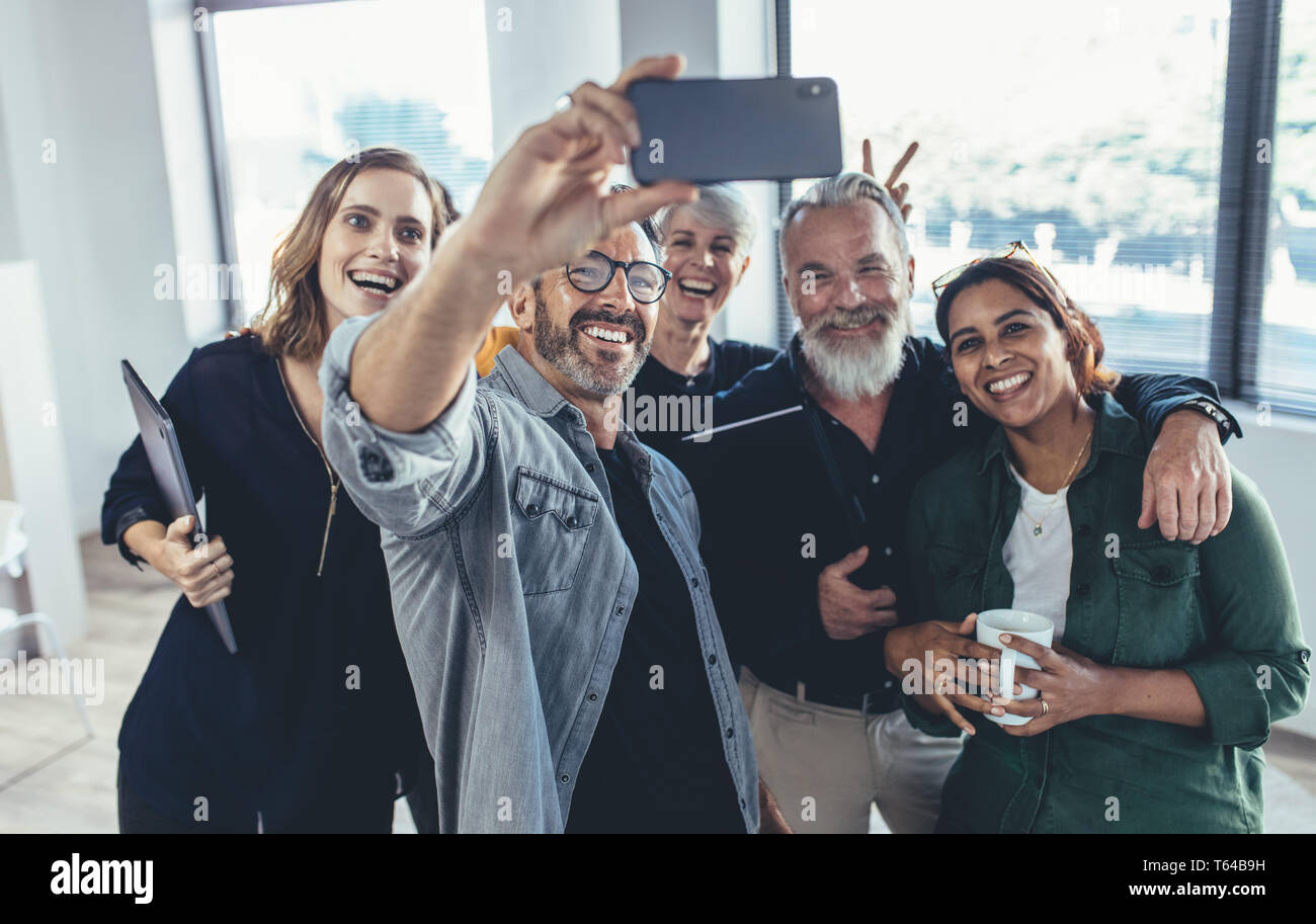 Fröhliche multiethnische Leute im Büro lächeln und das Selfie machen. Geschäftsmann macht Selfie mit seinen Kollegen im Büro. Stockfoto