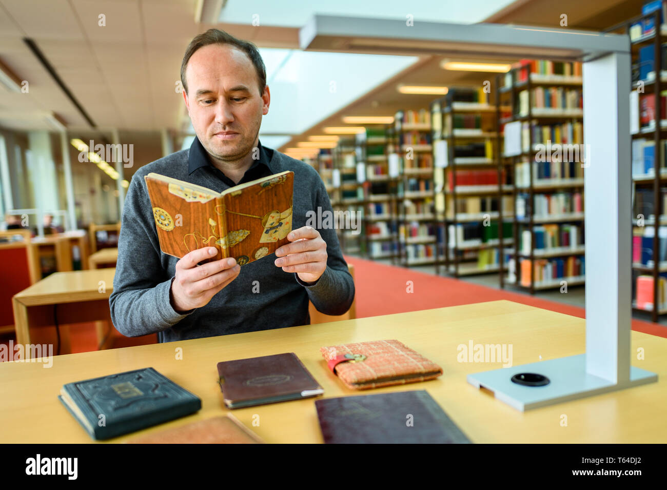 Oldenburg, Deutschland. 11 Apr, 2019. Stefan Walter, wissenschaftlicher Mitarbeiter am Institut für Pädagogik an der Carl-von-Ossietzky-Universität in Oldenburg, sitzt in einer Bibliothek und betrachtet ein Poesie Album. Walter hat recherchiert und seine Dissertation über Poesie Alben geschrieben. Credit: mohssen Assanimoghaddam/dpa/Alamy leben Nachrichten Stockfoto