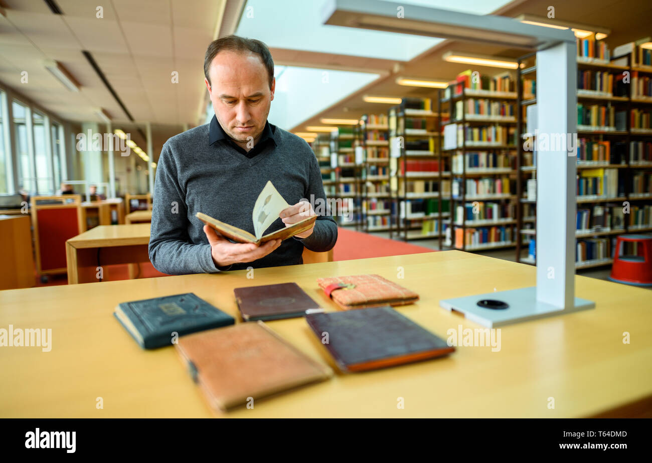 Oldenburg, Deutschland. 11 Apr, 2019. Stefan Walter, wissenschaftlicher Mitarbeiter am Institut für Pädagogik an der Carl-von-Ossietzky-Universität in Oldenburg, sitzt in einer Bibliothek und betrachtet ein Poesie Album. Walter hat recherchiert und seine Dissertation über Poesie Alben geschrieben. Credit: mohssen Assanimoghaddam/dpa/Alamy leben Nachrichten Stockfoto