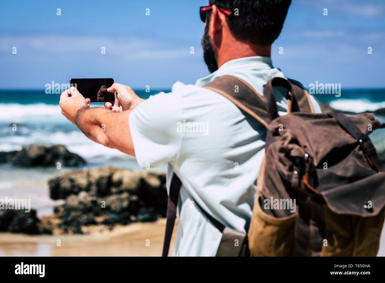 Kaukasische Mann mit Rucksack mit Mobile Phone Technology Gerät an den Strand und das Meer Wellen - Leute genießen reisen und hidd entdecken Stockfoto
