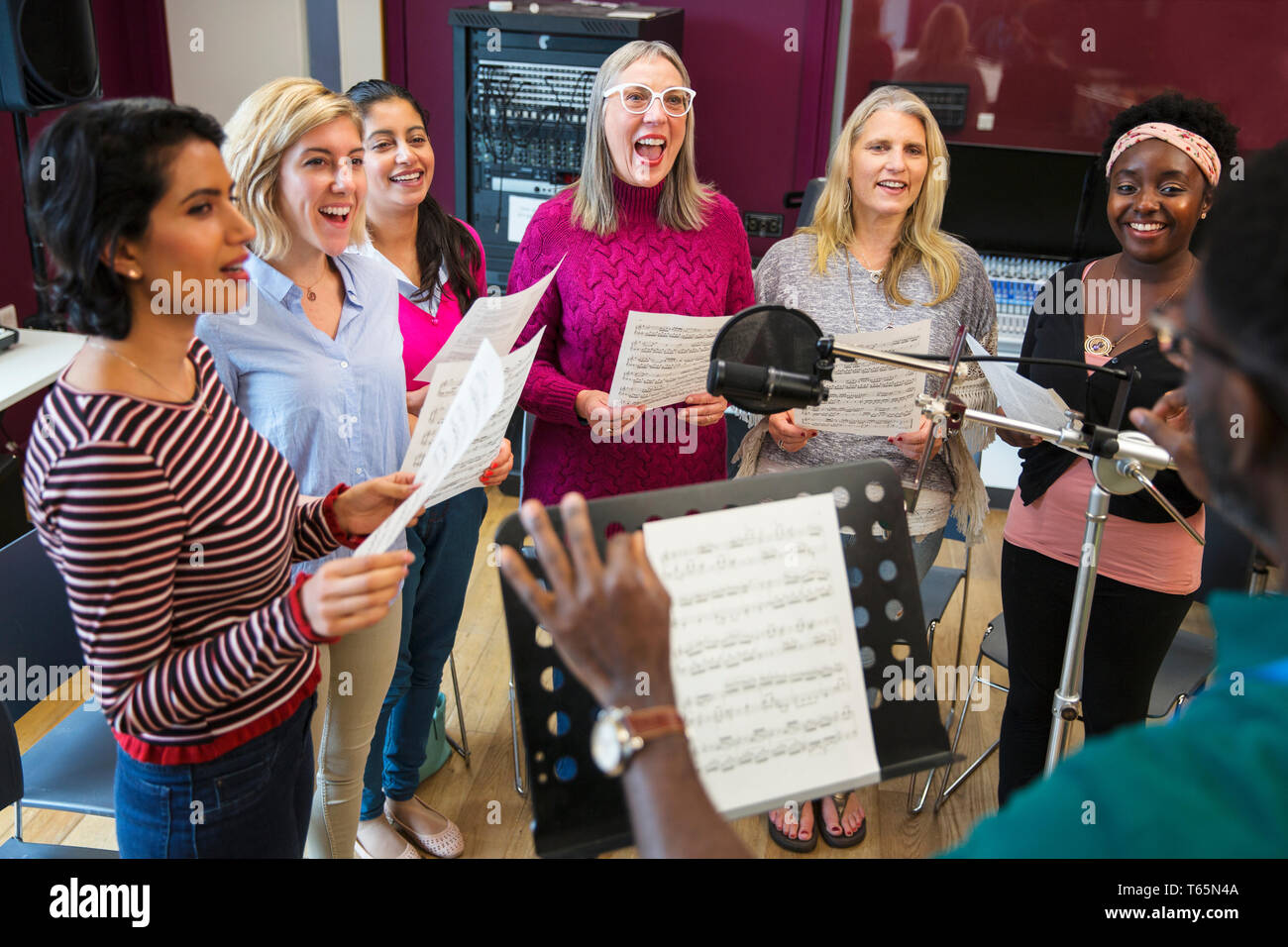 Männliche Leiter der führenden Frauen Chor mit Noten singen in Music Recording Studio Stockfoto