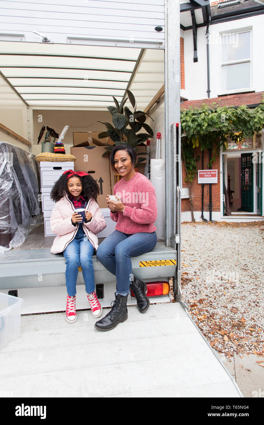 Portrait glückliche Mutter und Tochter trinkt Tee, eine Pause an der Rückseite des Moving van außerhalb neues Haus Stockfoto