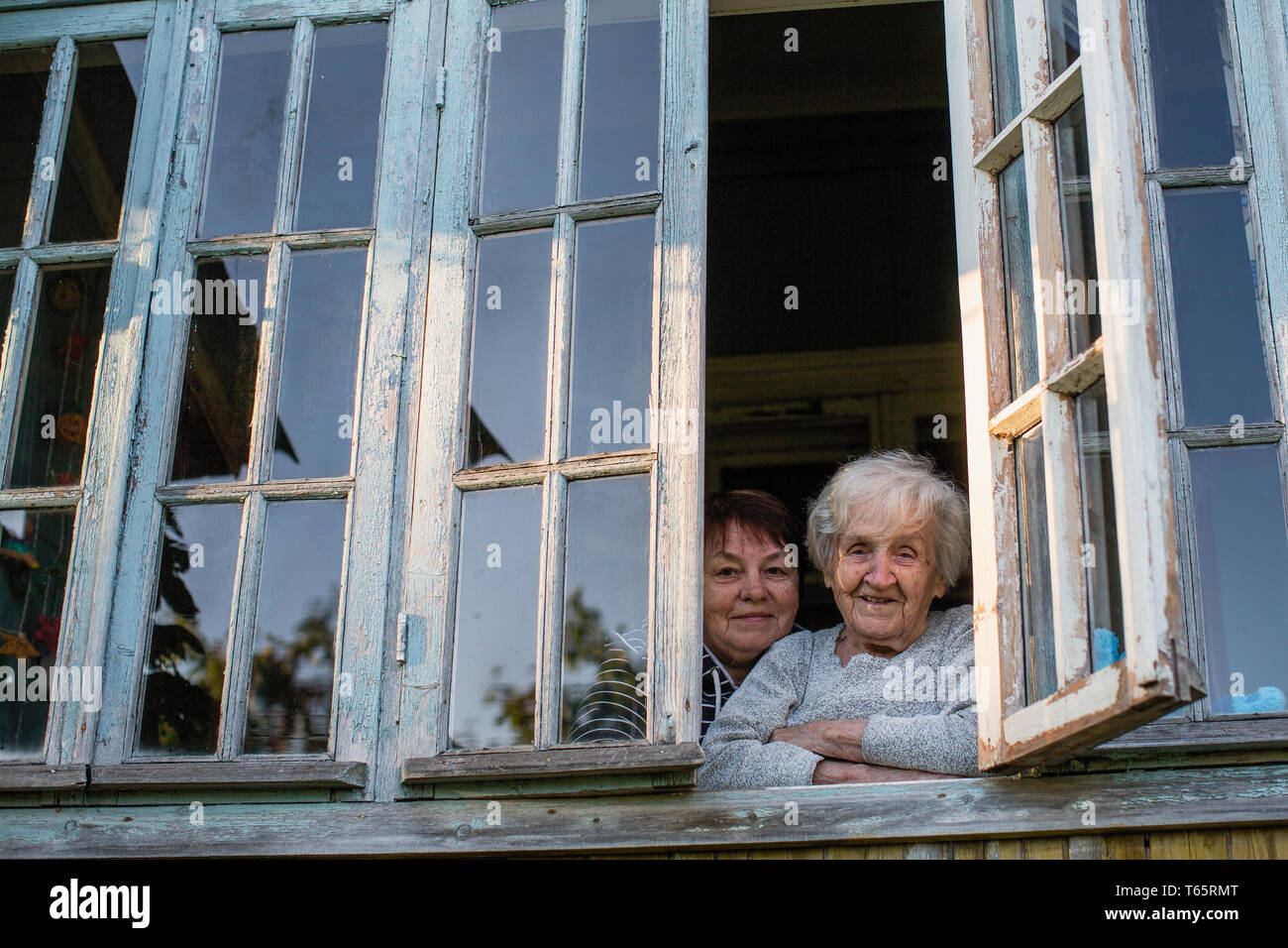 Eine alte Frau mit ihrer erwachsenen Tochter Blick aus dem Fenster von einem Haus im Dorf. Stockfoto